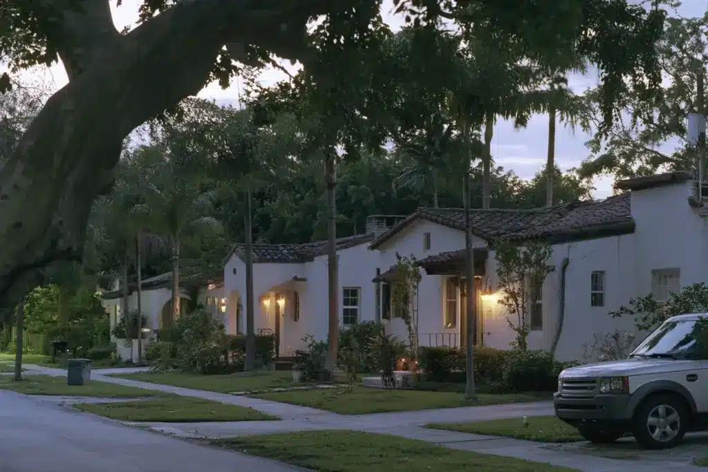 Row of Mediterranean-revival homes on a palm-shaded Coral Gables street at dusk with porch lights on