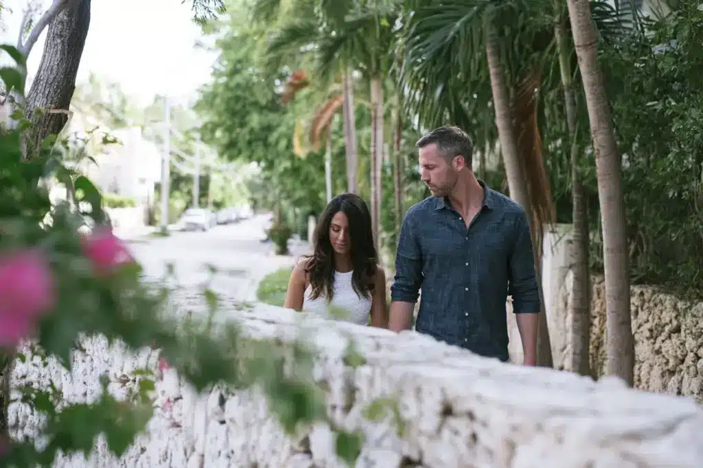 A Latina woman and a white man walking together on a palm-shaded Coral Gables street