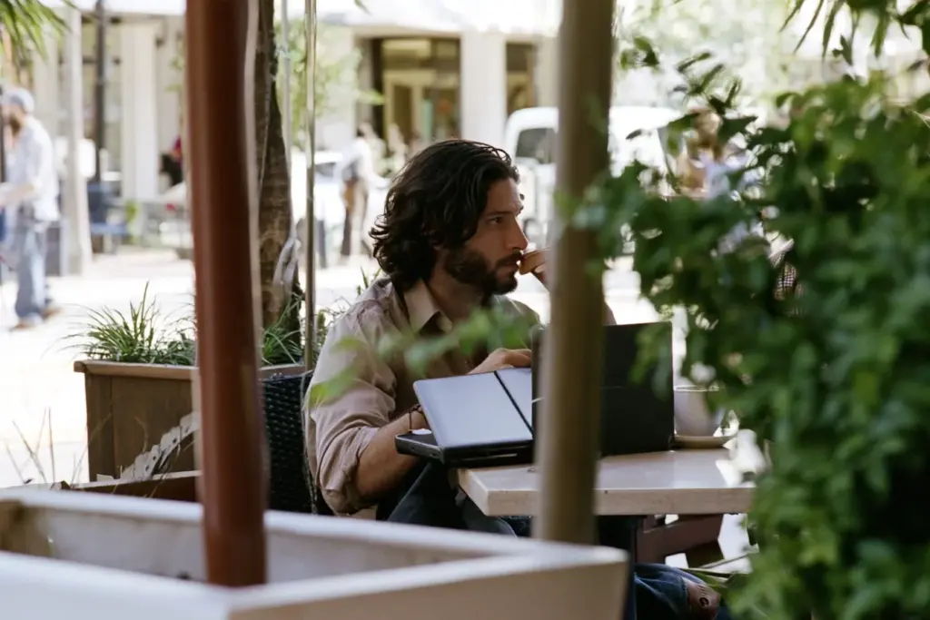 A man with dark wavy hair sitting alone at a café on Las Olas Boulevard, watching people pass