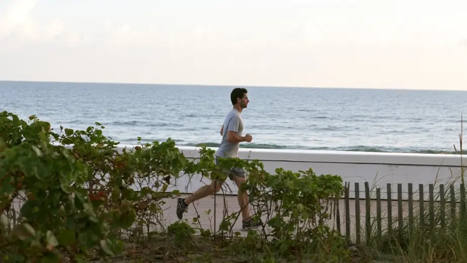 A man walking alone on a quiet Fort Lauderdale beach path at dawn under overcast light