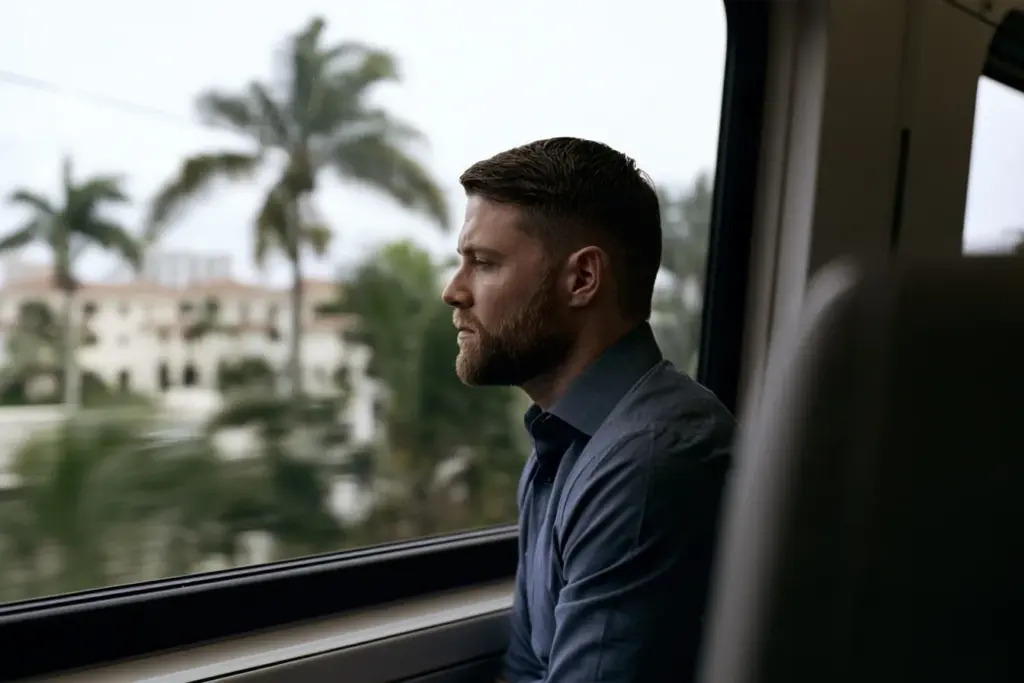 A man in a fitted shirt looking out the window on a South Florida commuter train