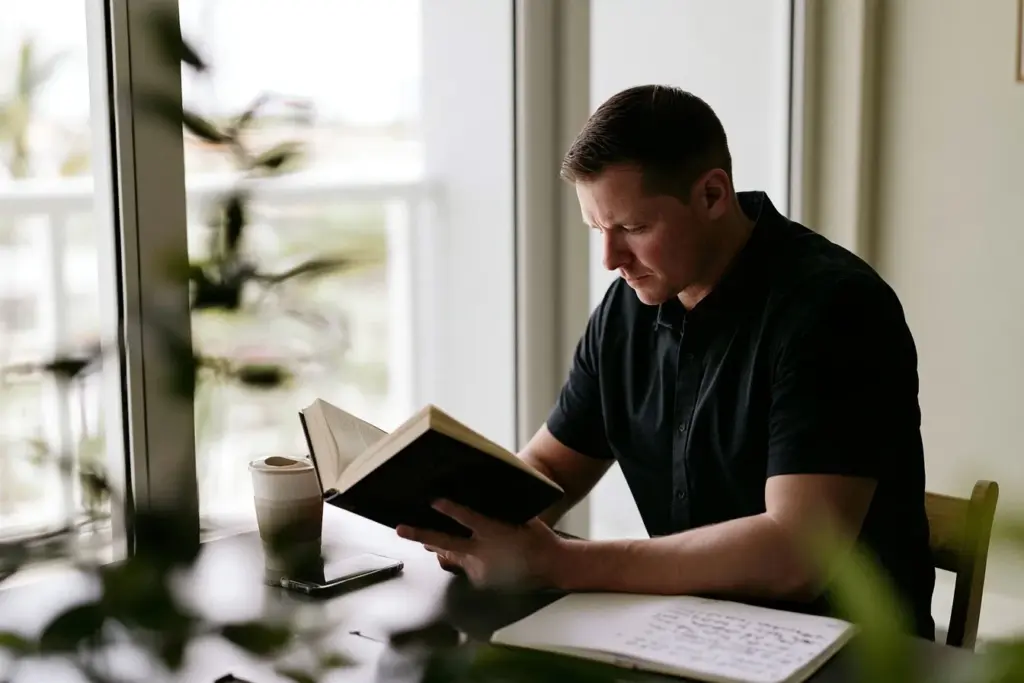 A man reading at a desk in a minimalist Las Olas condo in the morning with his phone face down