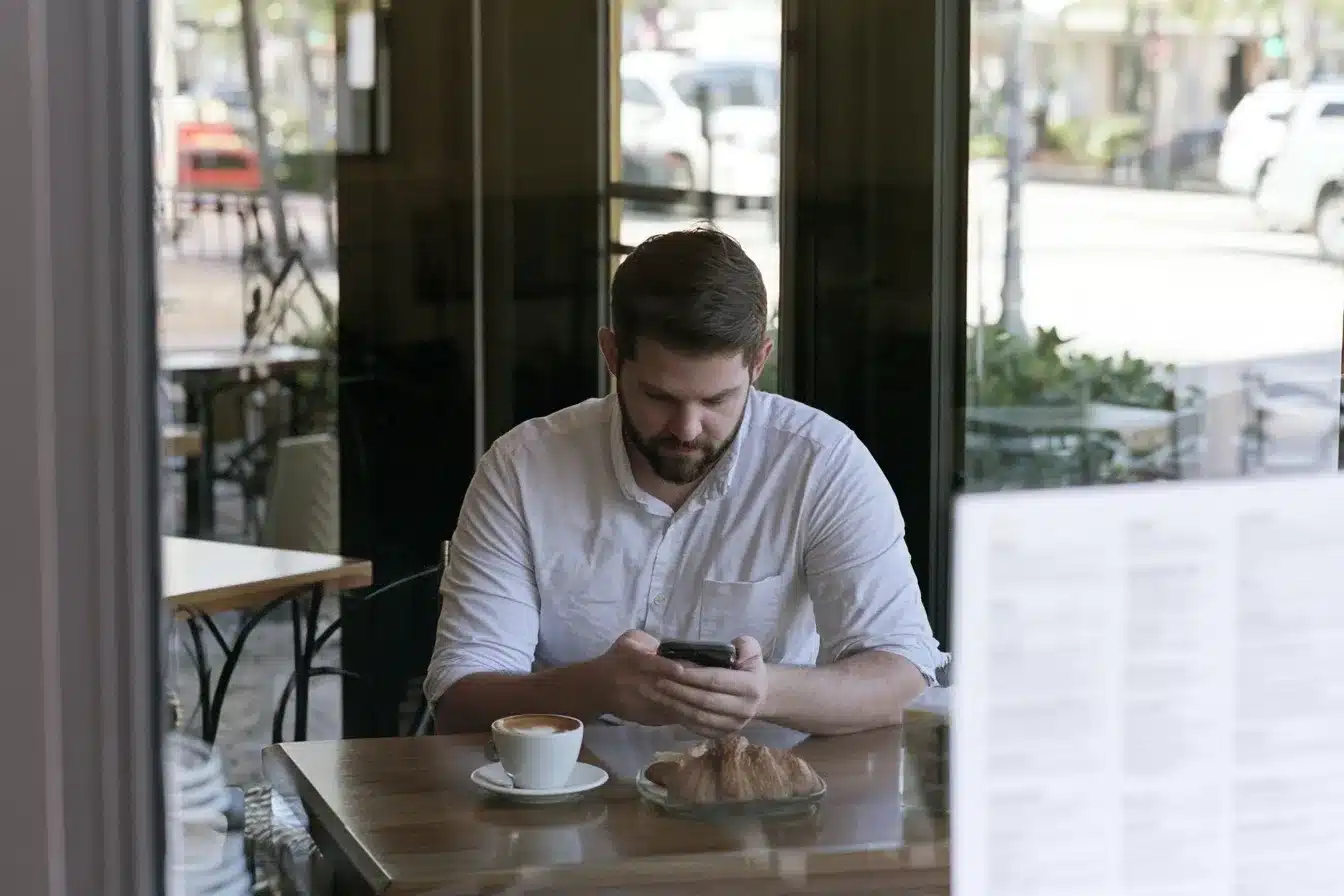 A man scheduling a consultation on his phone at a café on Las Olas Boulevard in the morning