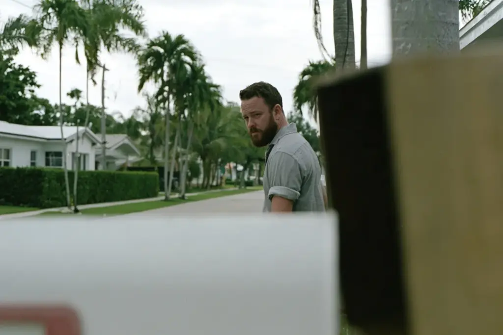 A man in his thirties walking alone on a quiet palm-lined Victoria Park street in Fort Lauderdale