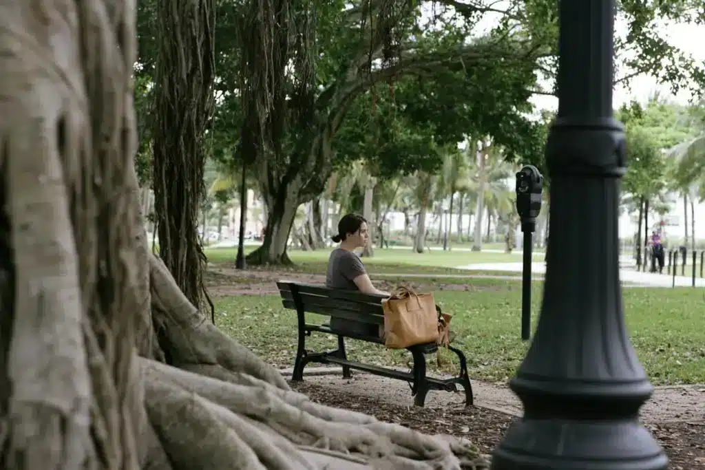 A woman sitting alone on a bench in a shaded Fort Lauderdale park, reflecting